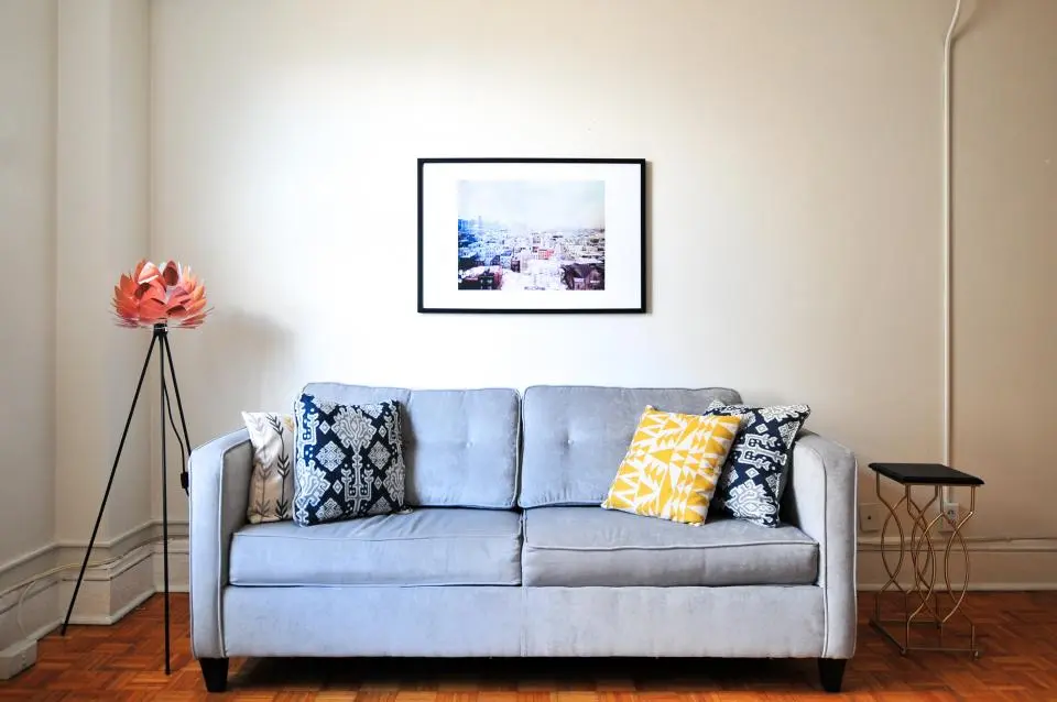 A pale blue sofa against a plain wall with a framed print