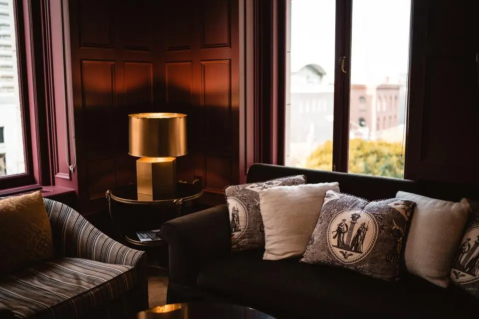 A dark snug with a sofa, cushions and a brass table lamp