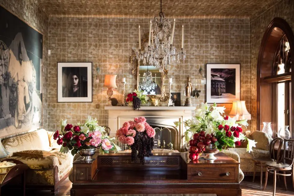 An eclectic drawing room with a chandelier, flowers and a brick wall