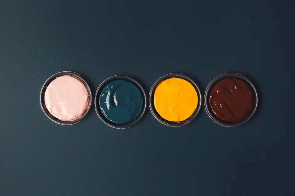 Four open tins of paint in pink, teal, saffron and oxblood