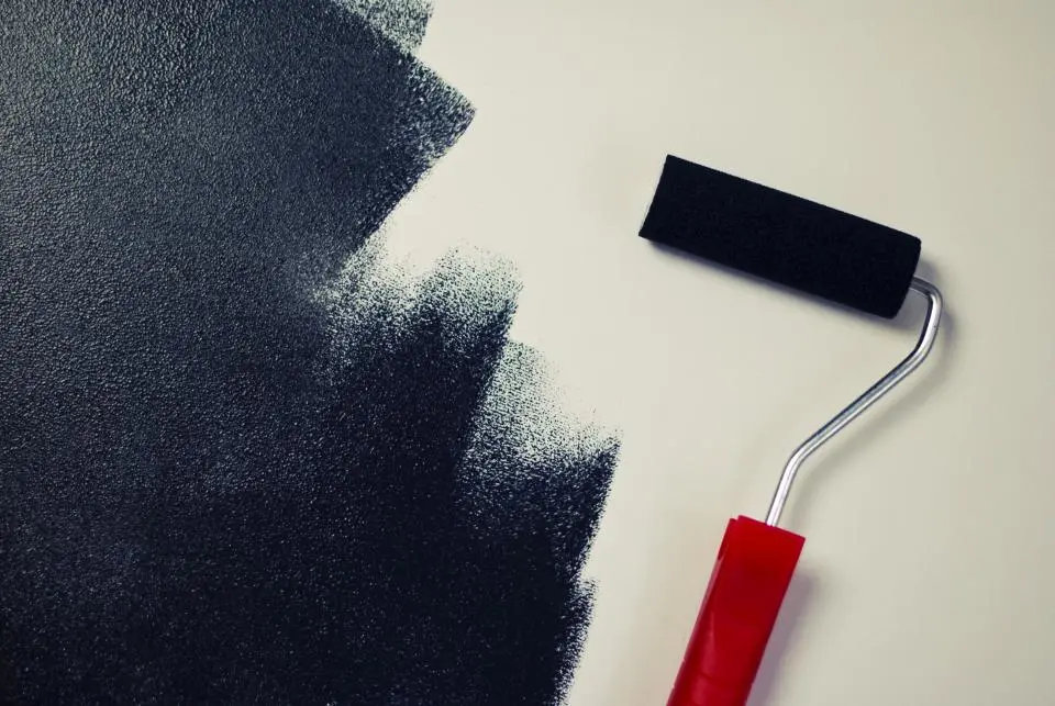 A paint roller applying dark paint to a wall