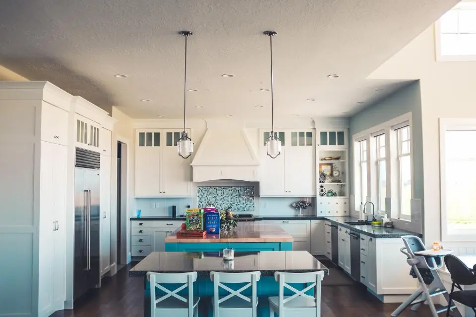 A white kitchen with a painted island and blue bar stools