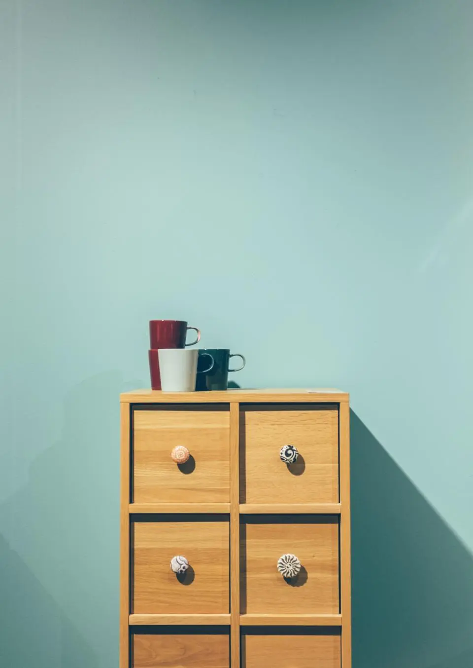 A teal painted wall behind a small wooden chest of drawers
