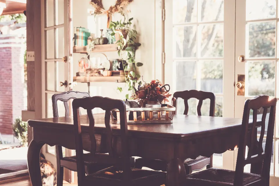 A dining room with dark carved chairs and sunlight from tall windows