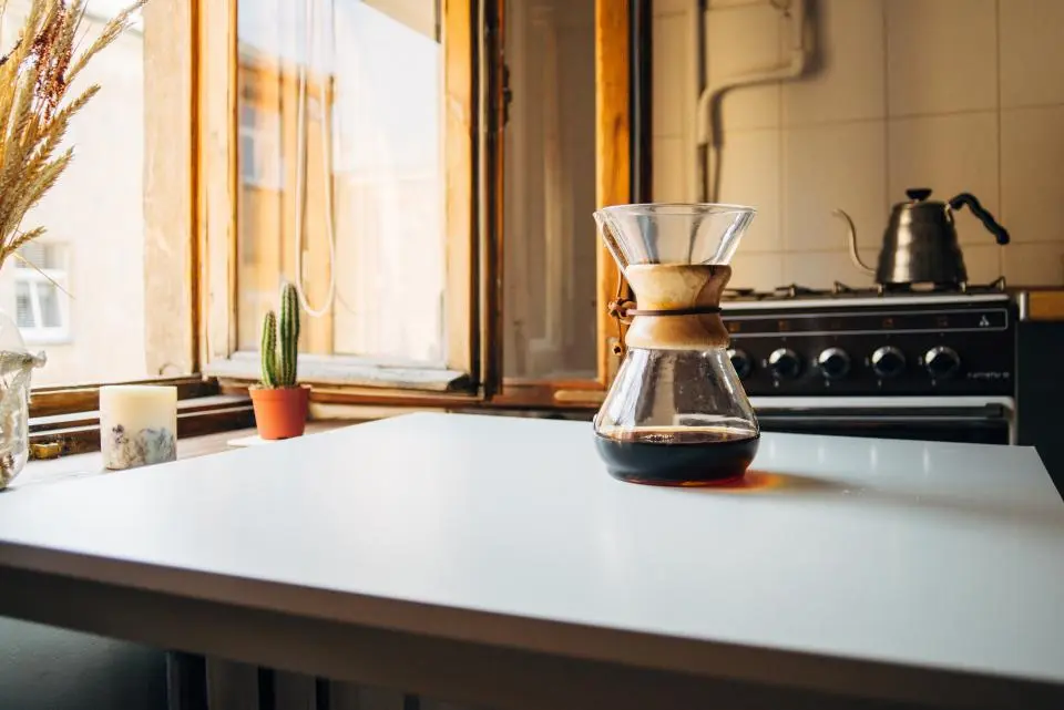 A kitchen worktop in warm window light with a coffee maker and a range cooker